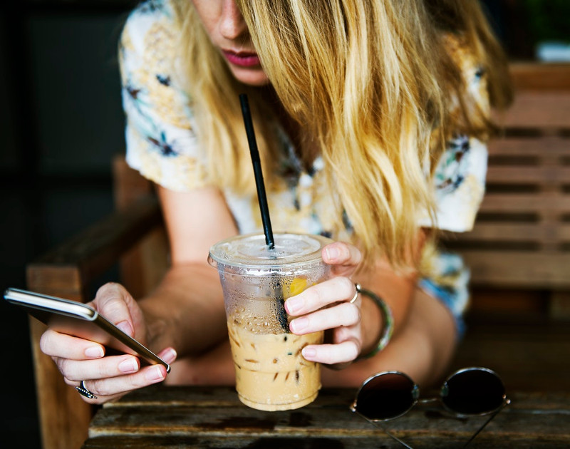 a woman drinking iced beverage and looking at her phone in a cafe