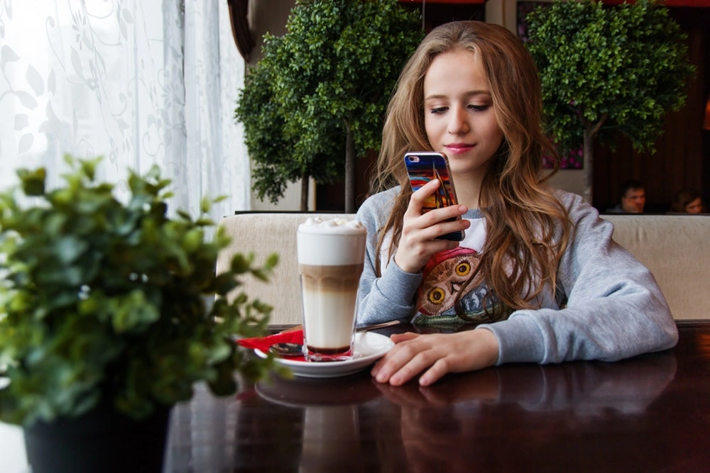 młoda kobieta siedząca przy stoliku i patrząca na telefon